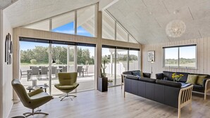 Un vaste espace de vie avec une grande porte-fenêtre coulissante donnant sur une terrasse extérieure, un canapé en cuir foncé et un fauteuil moderne.