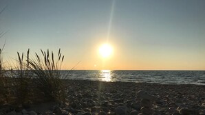 A beach with pebbles and grass in the foreground, and the sun setting over the water. - VillaVilla 321 - Gilleleje, Nordsjælland (Dronningmølle)