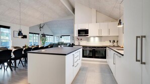 Una cocina moderna con armarios blancos, una isla central y una zona de comedor con sillas negras.