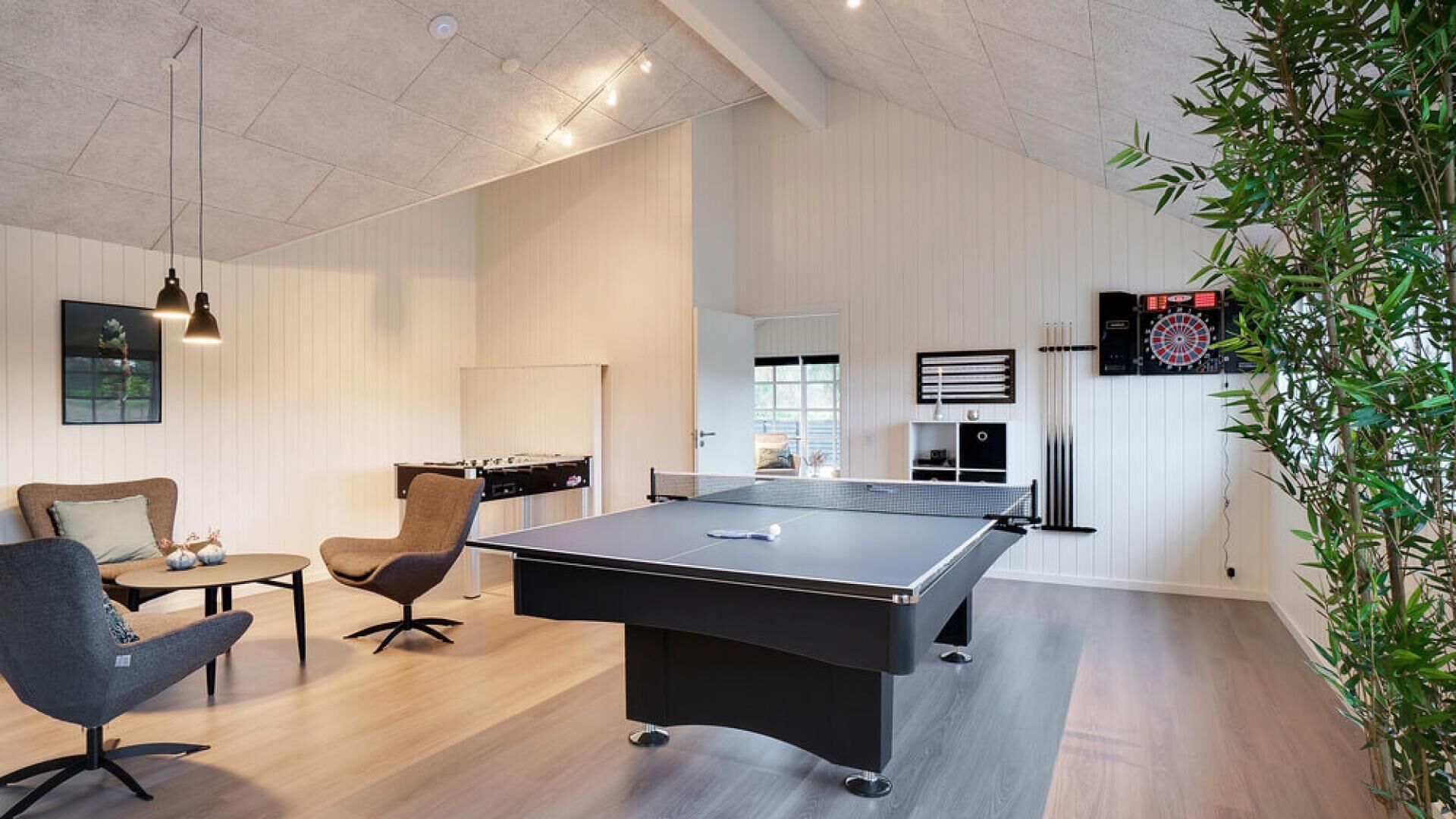 A modern room with a ping pong table, a dartboard, and a foosball table.
