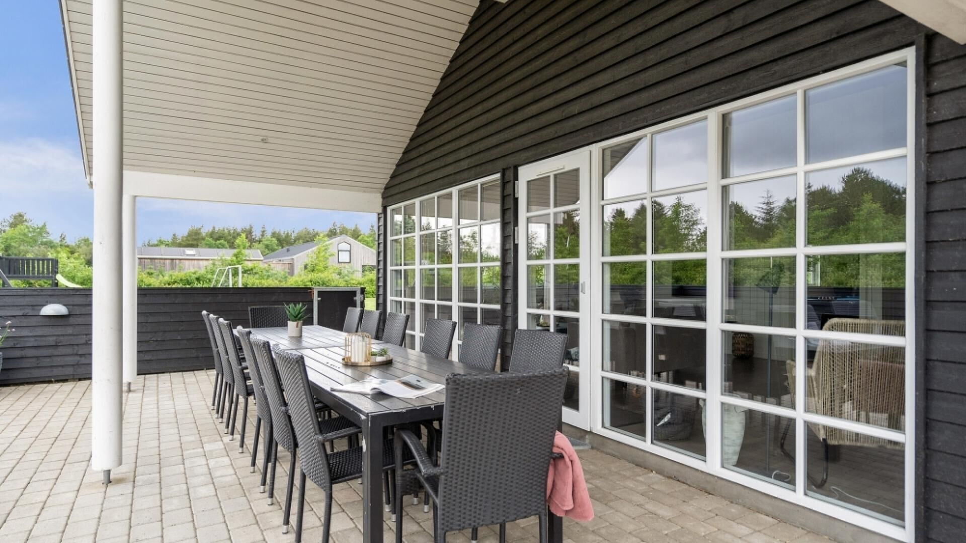 A covered patio with a dining table and chairs, large windows, and a view of the surrounding area.