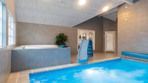 Una piscina interior con tobogán, un jacuzzi y una puerta que da a otra habitación.