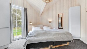 A bedroom with a bed, a nightstand, a wall-mounted light, a mirror, and a sliding glass door leading to a balcony. - VillaVilla 570 - Blåvand, Vestjylland (Blåvand)