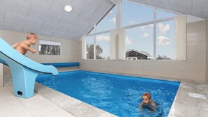 An indoor swimming pool with a blue slide, large windows, and a view of a house outside. - VillaVilla 327 - Faaborg, Fyn og øer (Faaborg)