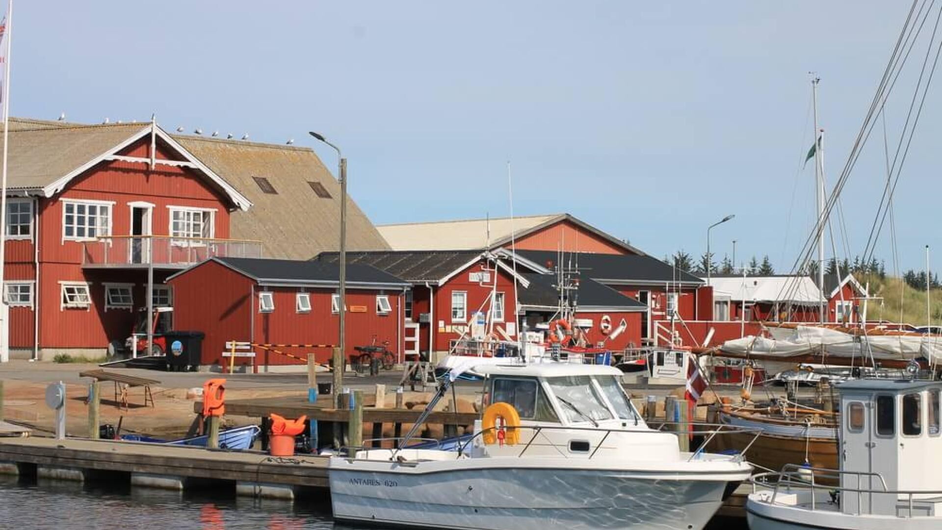 A marina with red buildings, boats docked, and a clear sky.