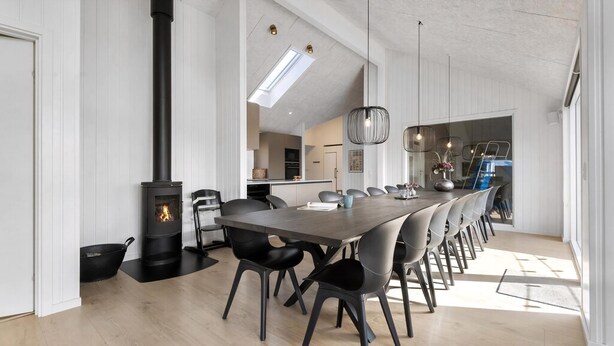 Eine moderne Küche mit einer zentralen Kochinsel, einem Essbereich mit einem langen Tisch und Stühlen sowie einem sichtbaren Kamin.