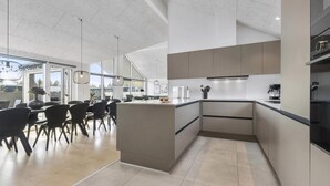 Eine moderne Küche mit Kochinsel, Essbereich mit Stühlen und großen Fenstern.