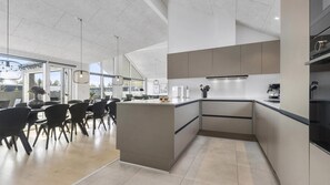 A modern kitchen with a central island, dining area with chairs, and large windows. - VillaVilla 560 - Houstrup Strand, Vestjylland (Nørre Nebel)