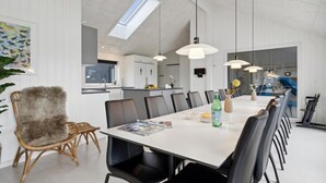 Uma sala de jantar moderna com uma mesa comprida, cadeiras pretas e luminárias pendentes.