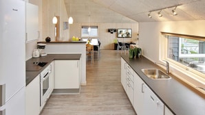 A modern kitchen with a central island, built-in appliances, and a dining area with a TV. - VillaVilla 296 - Kegnæs, Sydjylland (Sydals)