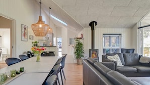 A modern living room with a grey sofa, a dining area with a white table, and a large window providing natural light. - VillaVilla 504 - Vejby Strand, Nordsjælland (Vejby)