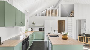 A modern kitchen with green cabinets, a wooden island, and a loft area with a staircase. - VillaVilla 251 - Marielyst, Lolland/Falster/møn (Idestrup)