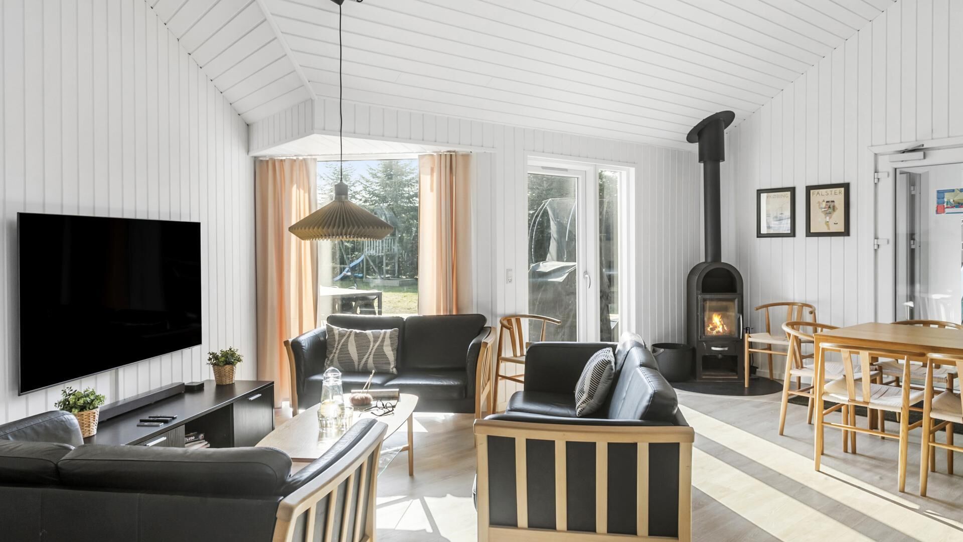 A modern living room with a flat-screen TV, leather sofas, a dining table, and a wood-burning stove.