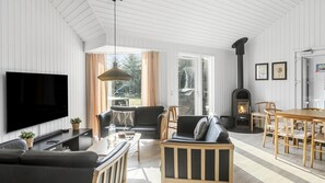 Ein modernes Wohnzimmer mit Flachbildfernseher, Ledersofas, einem Esstisch und einem Kaminofen.