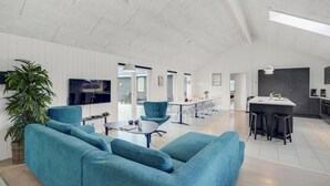 Ein geräumiger Wohnbereich mit einer großen Couch, einem Couchtisch und einem Fernseher. Es gibt eine Küchenzeile mit einer Bar und Hockern.