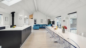 Eine moderne Küche mit einer zentralen Kochinsel, einem Essbereich mit einem langen Tisch und Stühlen, und einem blauen Sofa im Hintergrund.