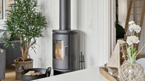 A modern living room with a wood-burning stove, a potted plant, and a wicker basket on the floor. - VillaVilla 644 - Østersøbadet, Lolland/Falster/Møn (Rødby)