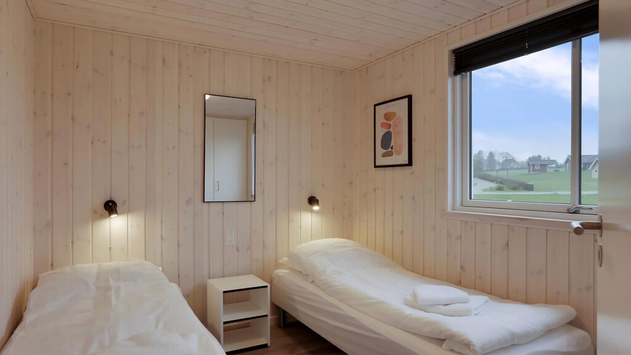 Una habitación con dos camas, una mesita de noche, un espejo y una ventana con vistas al paisaje.
