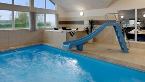 An indoor swimming pool with a blue slide, a reception desk, and a view of the outdoors through large windows. - VillaVilla 392 - Faaborg, Fyn og øer (Faaborg)