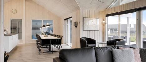 A modern interior with a dining area, a sofa, and large windows.