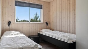A room with two beds, a small table, and a window with blinds. - VillaVilla 314 - Marielyst, Lolland/Falster/møn (Væggerløse)