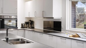 A modern kitchen with stainless steel appliances, a built-in oven, a coffee maker, and a window with a view of the outside. - VillaVilla 314 - Marielyst, Lolland/Falster/møn (Væggerløse)