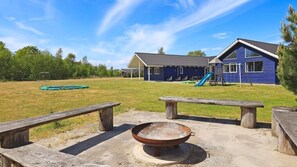 A backyard with a fire pit, picnic tables, a blue house with a slide, and a grassy field. - VillaVilla 314 - Marielyst, Lolland/Falster/møn (Væggerløse)
