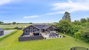 Une maison moderne dotée d’un grand patio, de panneaux solaires et offrant une vue sur la campagne environnante.