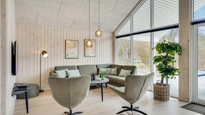 Un salon moderne avec un mur en bois, une grande fenêtre, un canapé gris, deux fauteuils, une table basse et une plante en pot.
