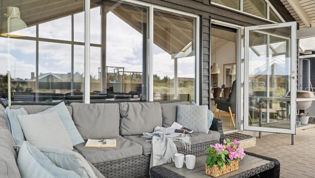 Un espace extérieur moderne aménagé avec un canapé, des coussins et une table basse agrémentée de fleurs.