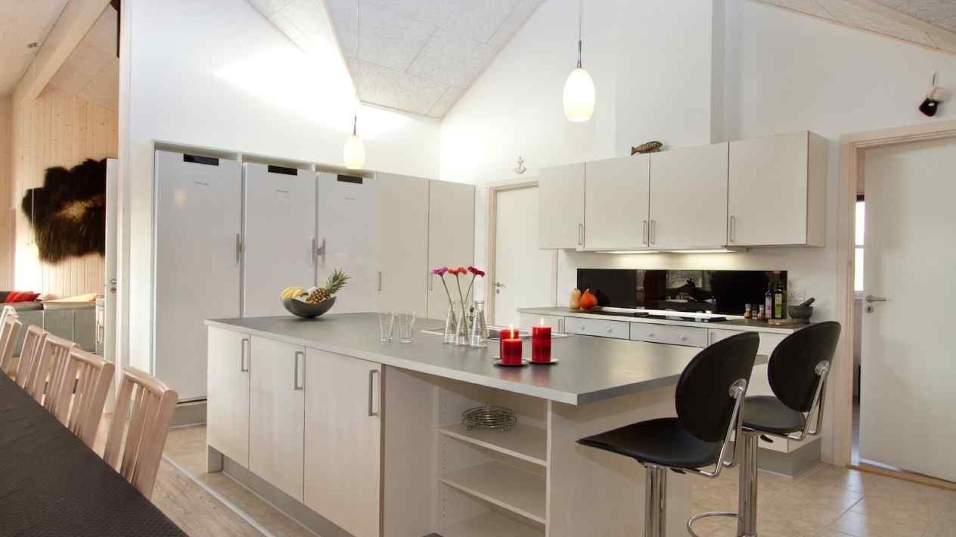 Una cucina moderna con mobili bianchi, un'isola centrale con sgabelli da bar e un lampadario a sospensione.