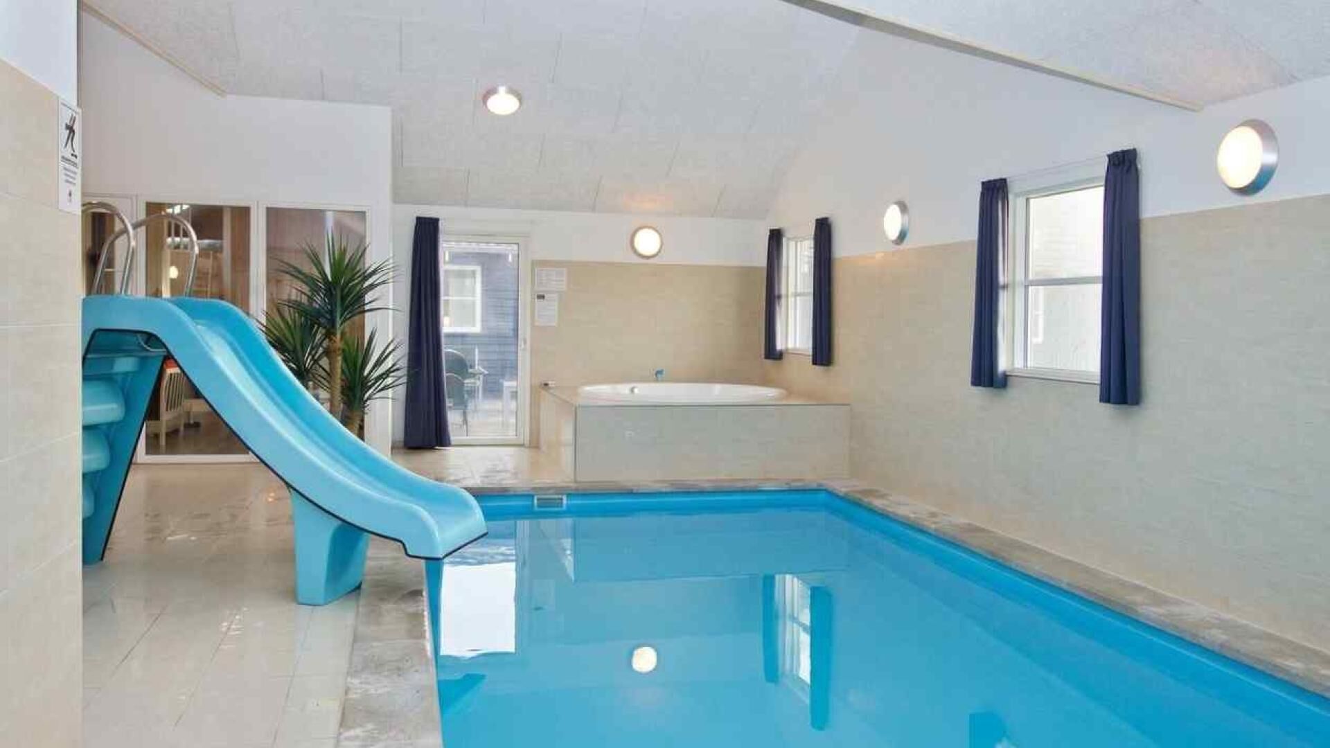 An indoor swimming pool with a blue slide, a bathtub, and a door leading to an outdoor area.