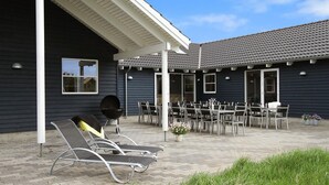A covered outdoor patio with lounge chairs, a barbecue grill, and a dining area with tables and chairs. - VillaVilla 283 - Vejers, Vestjylland (Vejers Strand)