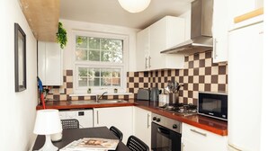 Una cucina compatta con mobili bianchi, un forno a microonde, un piano cottura a gas e un lavello.