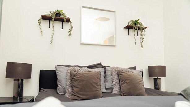 Camera moderna con un letto, due comodini, due lampade e due mensole a parete con piante.
