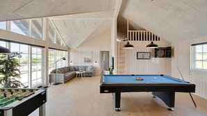 Une pièce spacieuse équipée d’une table de billard, d’un baby-foot, d’un canapé et d’une table de ping-pong. De grandes fenêtres laissent entrer la lumière naturelle et offrent une vue sur l’extérieur.