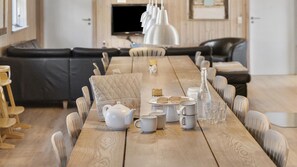 A dining table set with plates, glasses, and a teapot, surrounded by chairs in a room with a wooden floor and a black leather sofa in the background. - VillaVilla 247 - Ebeltoft, Østjylland (Ebeltoft)