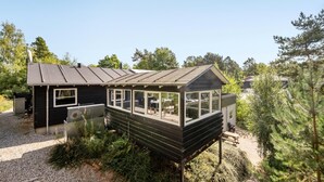 Une petite cabane avec un toit en pente, de grandes fenêtres et une véranda couverte.