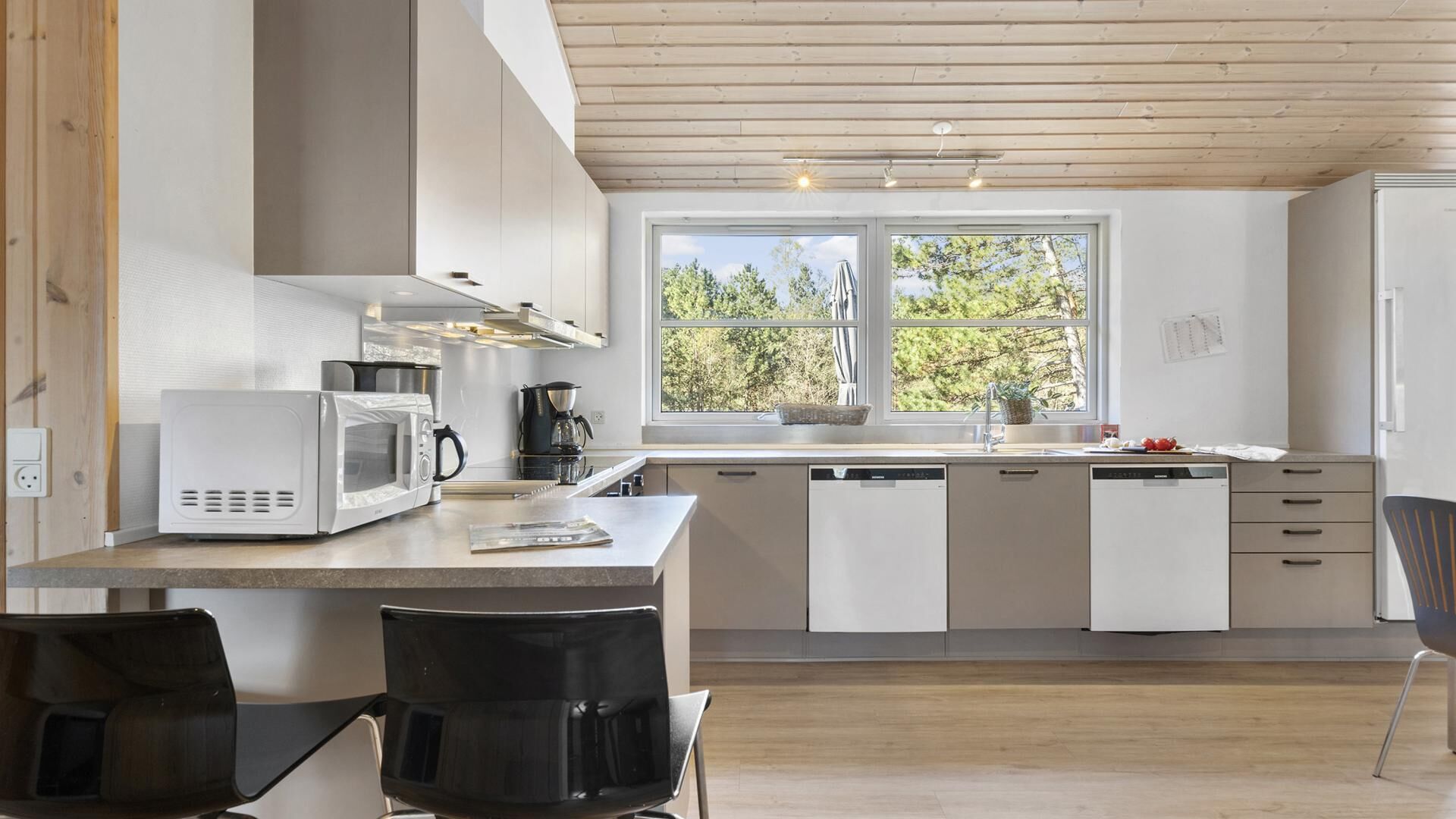 A modern kitchen with white cabinets, a microwave, a coffee maker, and a window with a view of trees.