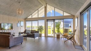 A spacious living room with a large TV, comfortable seating, and a view of the outdoors through large windows. - VillaVilla 428 - Skåstrup Strand, Fyn og øer (Bogense)
