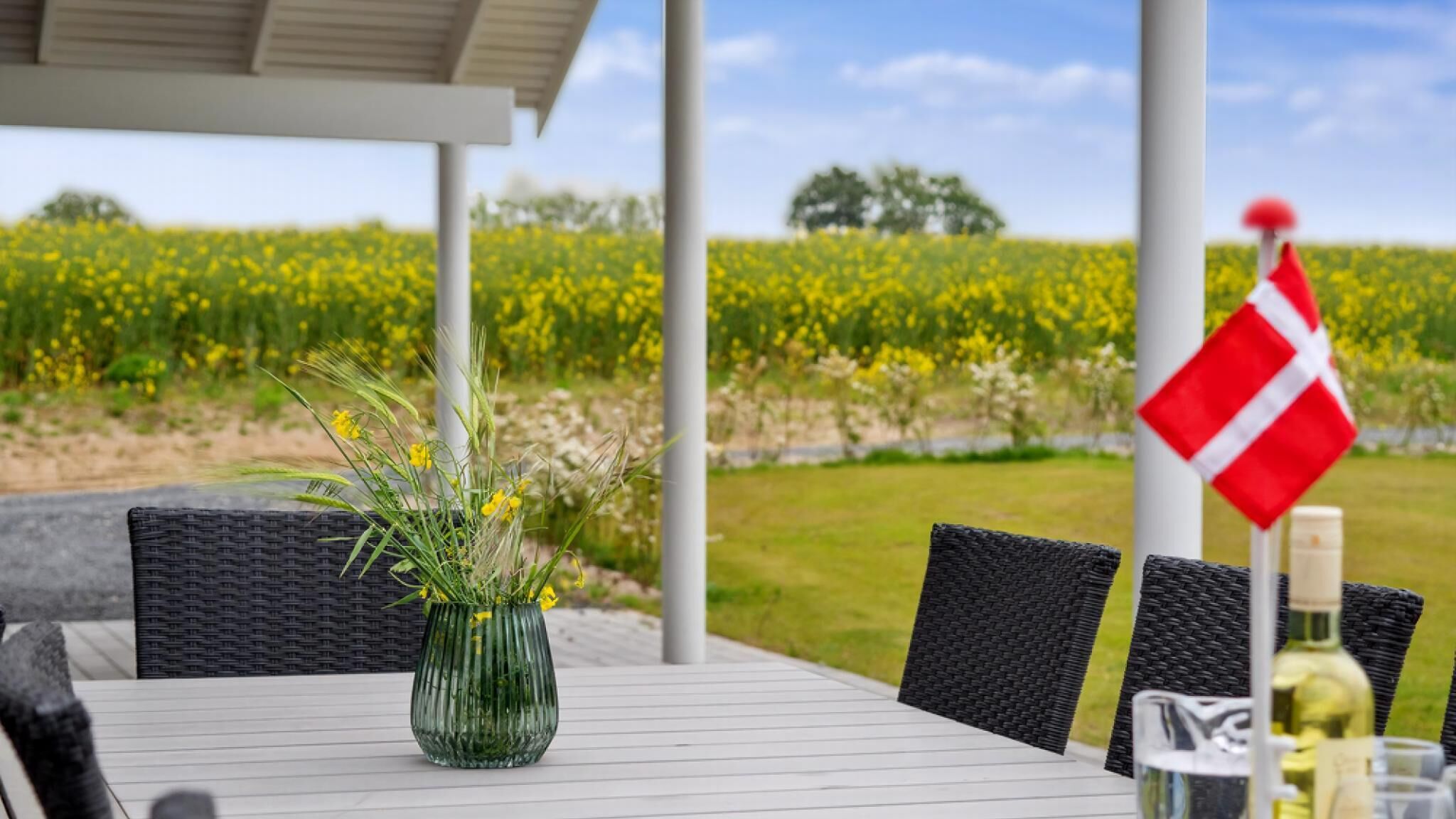 Et bord med en vase med gule blomster, en flaske og et dansk flag.