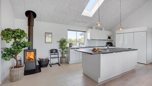 Eine moderne Küche mit Kochinsel, Kaminofen, weißen Schränken und einem Dachfenster.