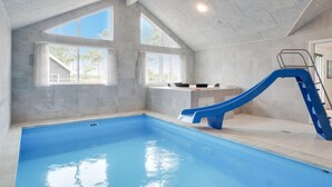 Une piscine intérieure avec un toboggan bleu, de grandes fenêtres et un coin cuisine.