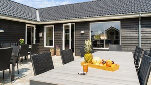Un patio al aire libre con una mesa lista para comer, rodeada de sillas y una cesta de fruta sobre la mesa.