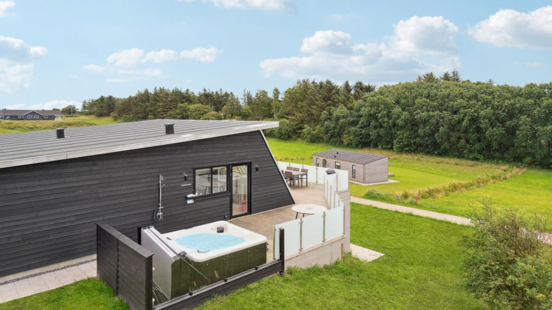 A modern house with a hot tub, outdoor seating, and a large garden.