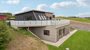 Uma casa moderna de dois andares com telhado plano, janelas grandes e área externa coberta.