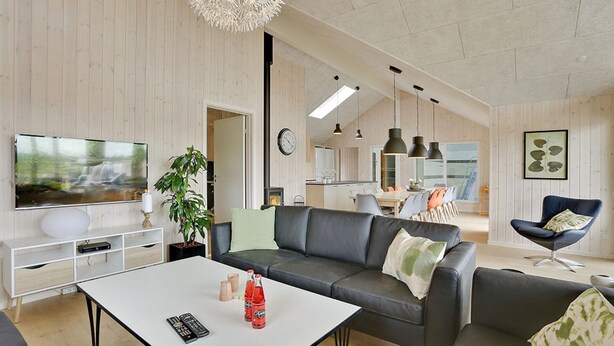Ein modernes Wohnzimmer mit Sofa, Couchtisch und Fernseher. Im Hintergrund befindet sich eine Pflanze, eine Uhr und ein Essbereich.