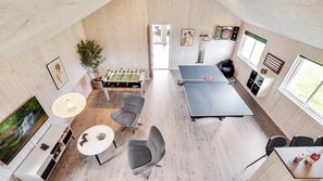 Ein geräumiger Raum mit Kicker, Tischtennisplatte und einem weiteren Kicker. Es gibt eine Essecke mit Tisch und Stühlen sowie ein großes Fenster für natürliches Licht.