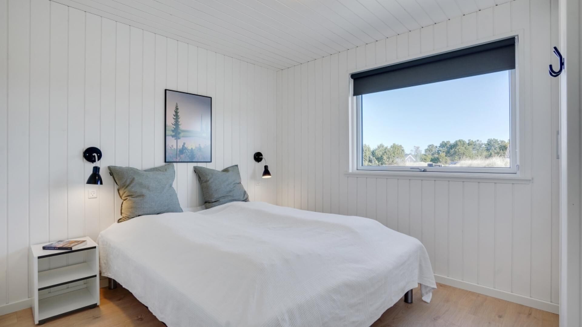 Une chambre à coucher avec un grand lit, deux tables de chevet, une commode, une fenêtre donnant sur un beau paysage et un tableau encadré au mur.