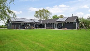 Ein großes, dunkel gefärbtes Gebäude mit flachem Dach und Solaranlagen, umgeben von einer Wiese und Bäumen.
